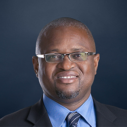 Vince Reid smiles to the camera against a dark blue background.